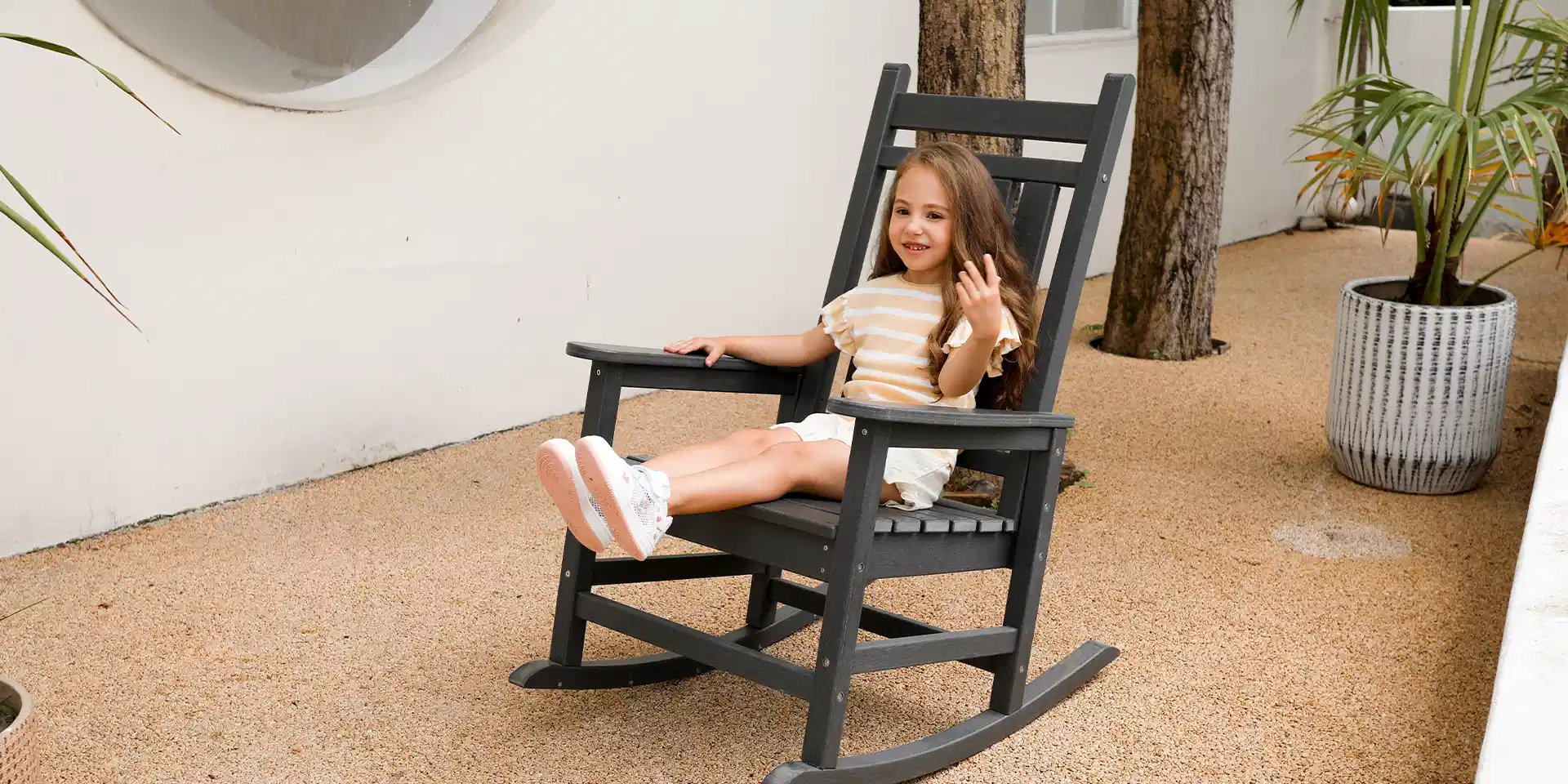 A little girl sitting on the black rocking chairs for front porch.