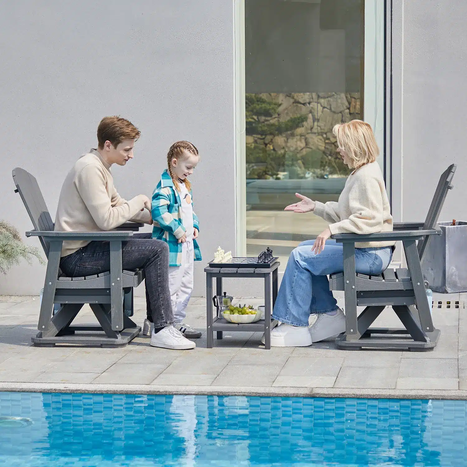A couple sitting on the outdoor swivel glider chair gplaying with their daughter by the pool side