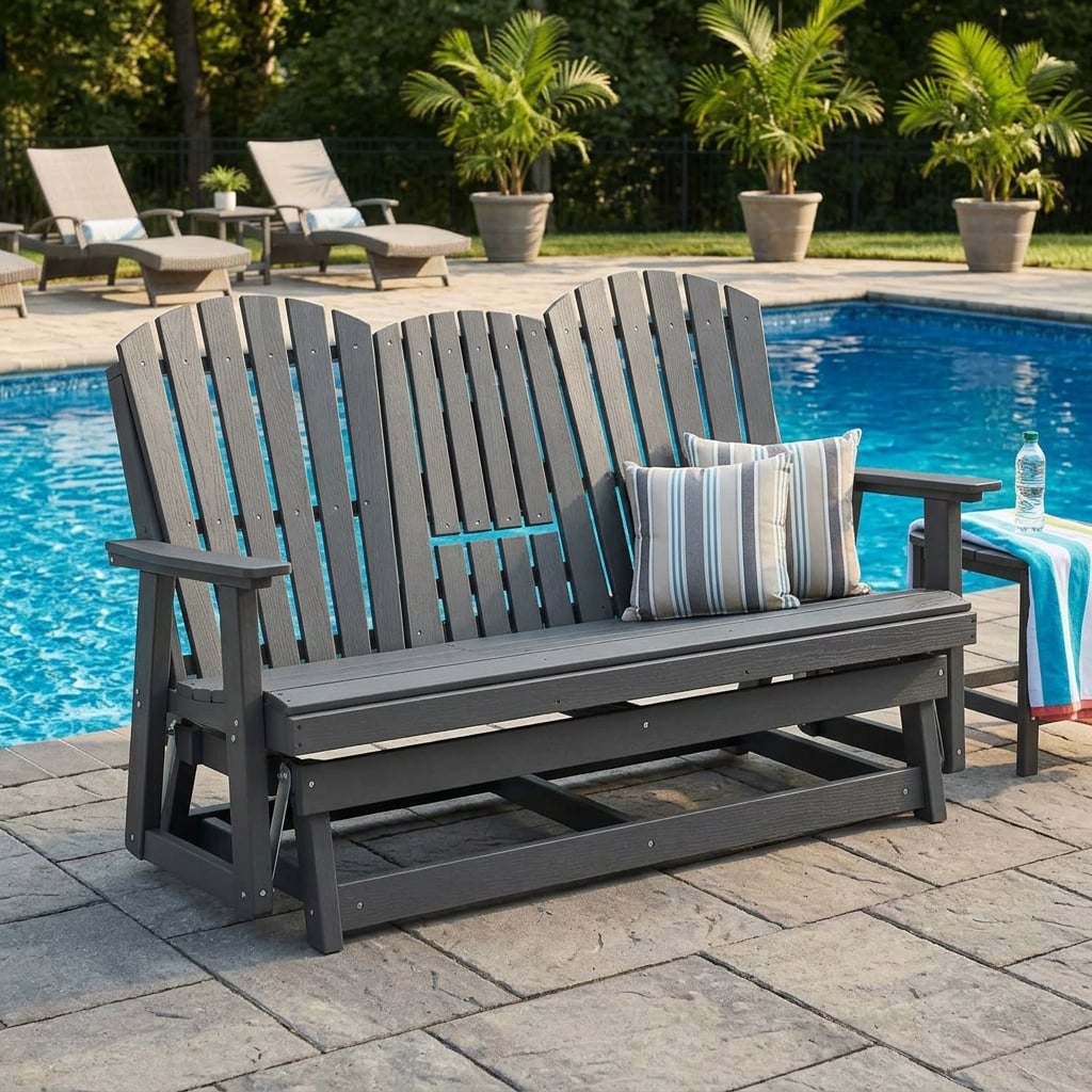 Charcoal gray HDPE Adirondack-style glider bench with slatted backrests, wide armrests, striped pillows, and wood-grain texture beside a backyard pool.